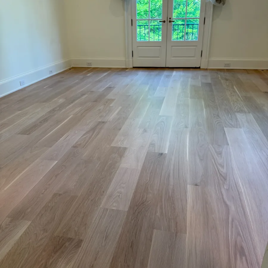 Empty room featuring new light oak hardwood flooring and white French doors with a green forest view.