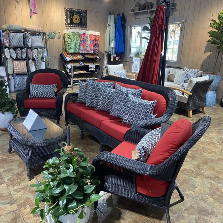 Indoor display of wicker patio furniture with red cushions, gray patterned pillows, and decorative plants in a showroom.