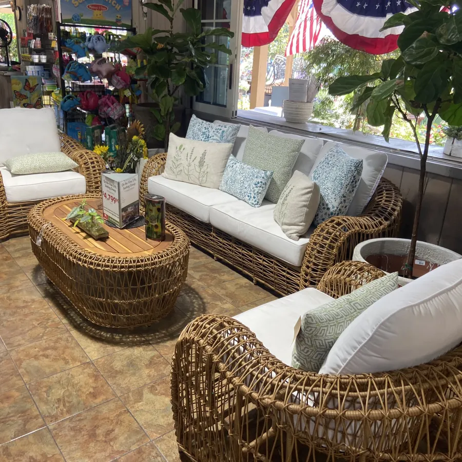 Rattan wicker sofa set with white cushions and patterned pillows around wooden coffee table on tiled floor.