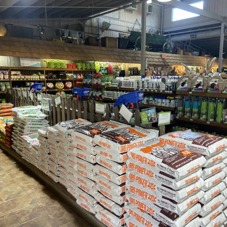 Indoor garden center with stacked bags of fertilizer, plant care products, and gardening tools on display.