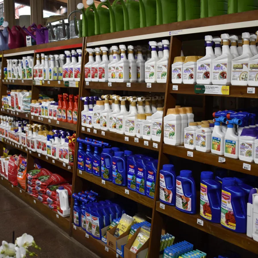 Shelves stocked with various garden care products including fertilizers, pest control sprays, and plant nutrients in a store.