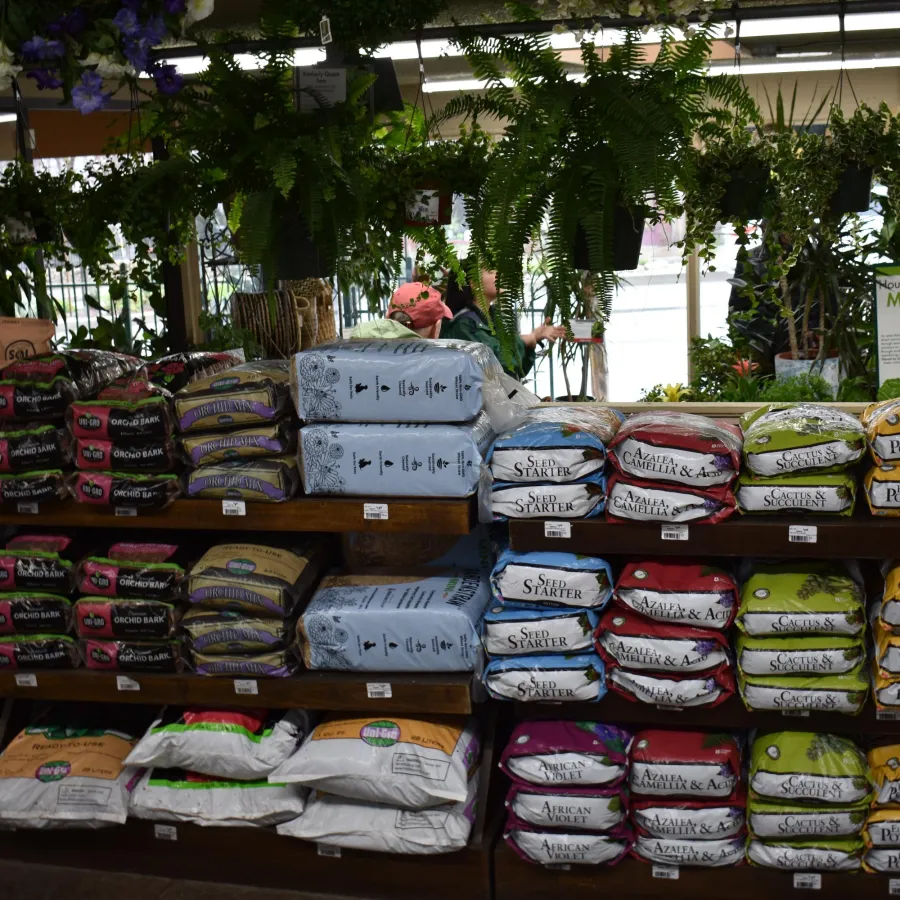 Shelves stocked with various bags of garden soil, seed starters, and potting soil in a garden center store.