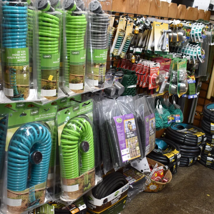 Garden hoses and outdoor hardware accessories displayed on wall racks and shelves in a store aisle.