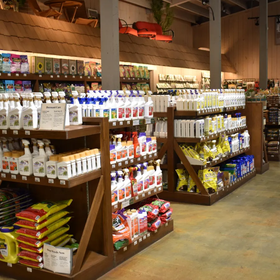 Garden supply store aisle with shelves stocked with fertilizers, sprays, and soil bags under warm lighting.
