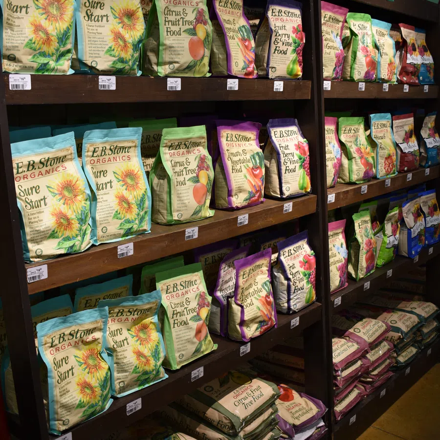 Shelves stocked with colorful E.B. Stone Organics plant food bags and watering cans on top in a garden store.