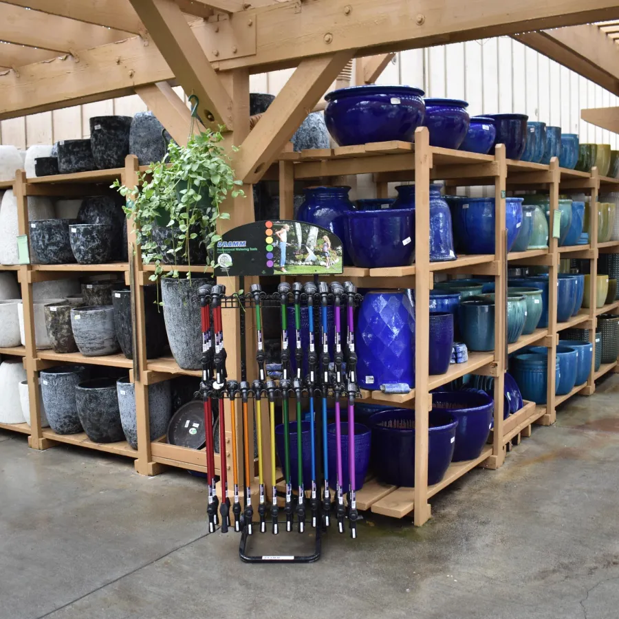 Wooden shelves filled with large ceramic pots in various colors inside a garden center with a concrete floor.