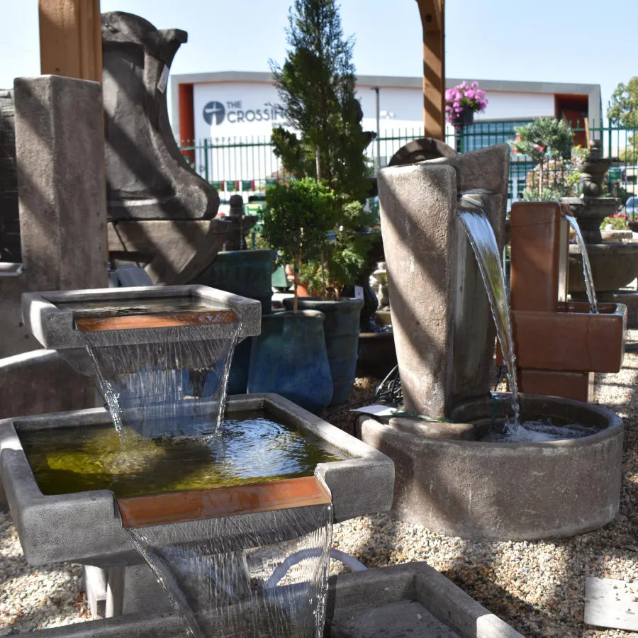 Outdoor display of cascading stone water fountains under a wooden pergola with plants and a building in the background