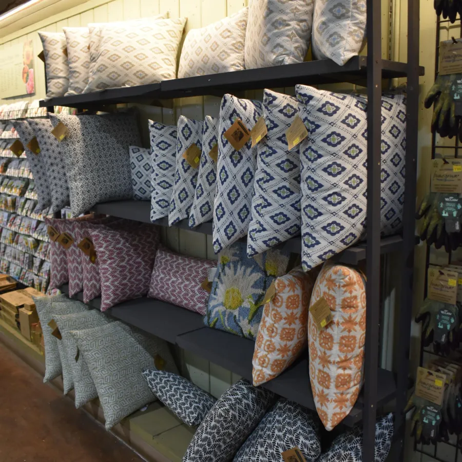 Decorative throw pillows with various patterns displayed on gray metal shelves in a store aisle.