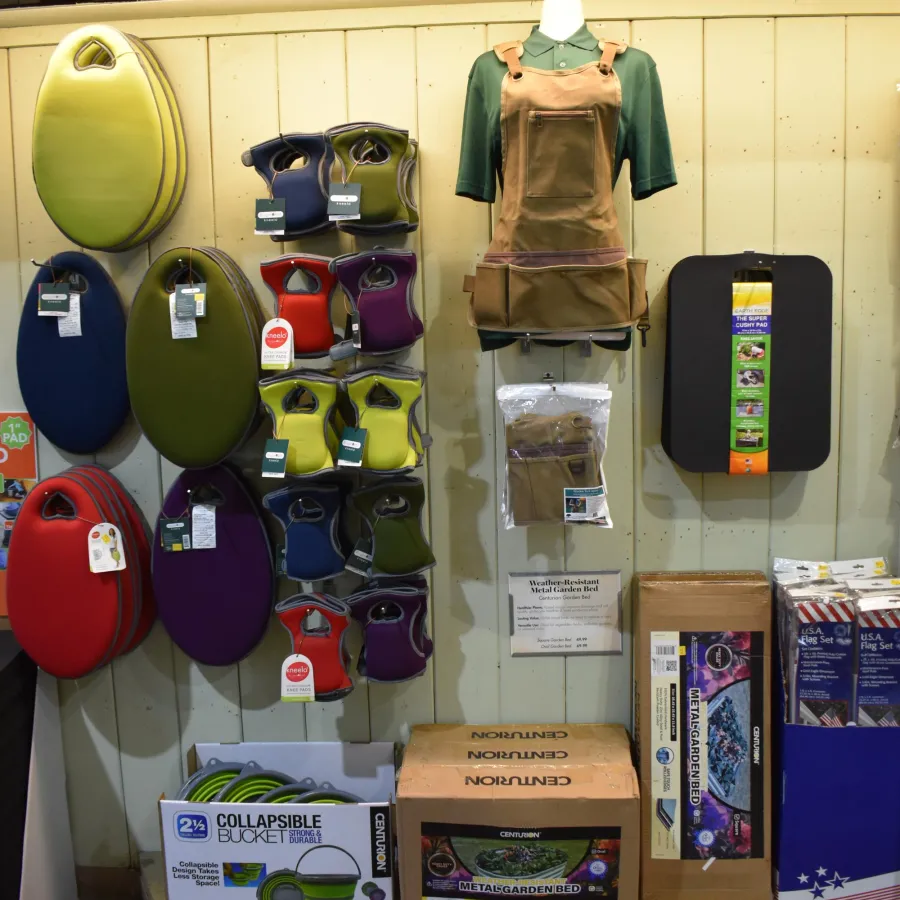 Wall display of garden kneeling pads, kneeling apron, collapsible bucket, and boxed metal garden bed kit.