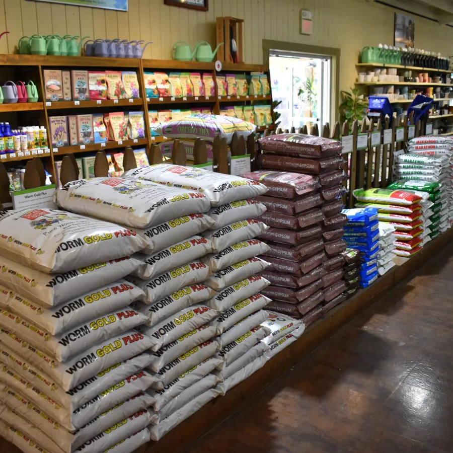 Stacks of gardening soil and potting mix bags displayed on wooden shelves inside a garden supply store.