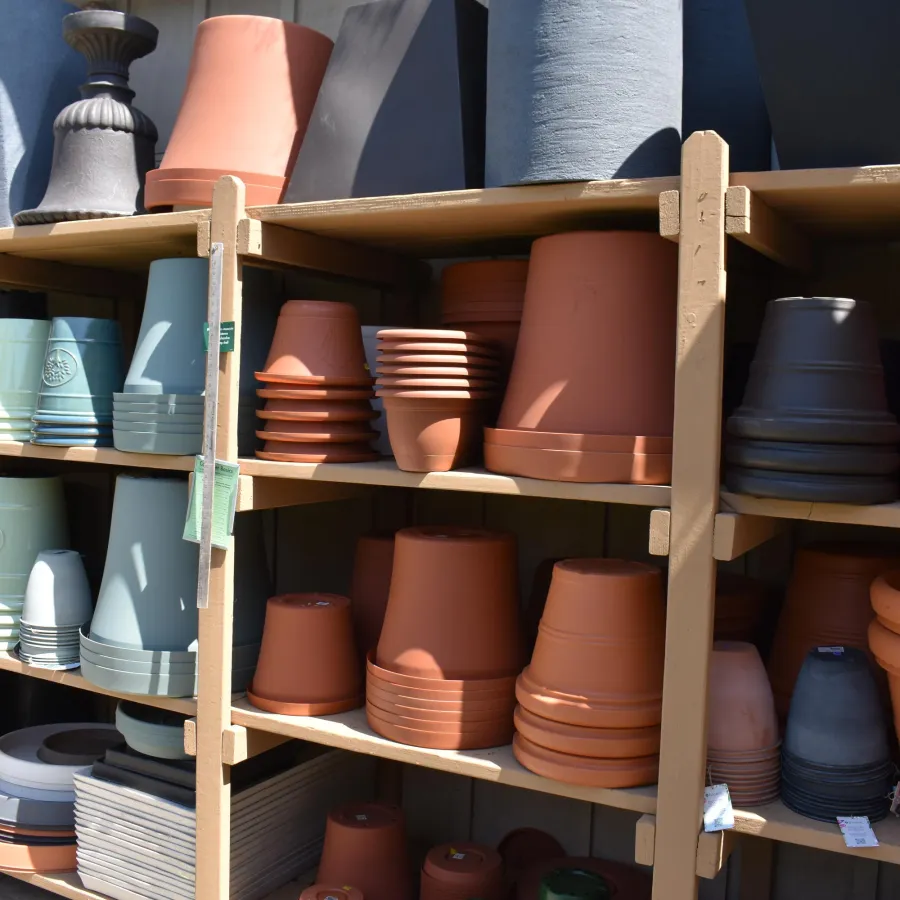 Shelves filled with various sizes and colors of stacked ceramic and plastic flower pots in a garden store.