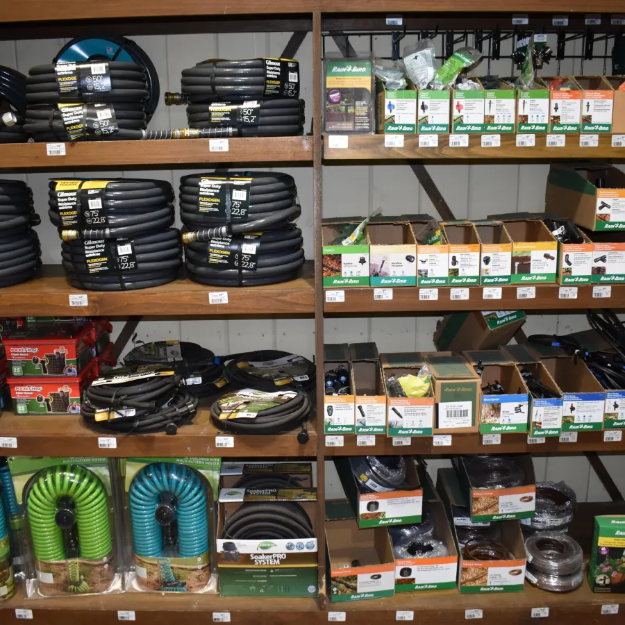Shelves stocked with coiled hoses, irrigation supplies, and garden hose accessories in a hardware store.