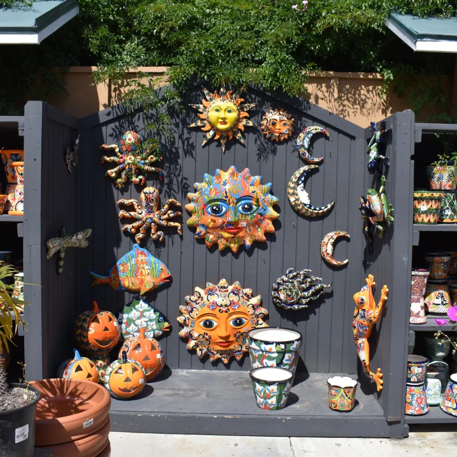 Colorful ceramic sun, moon, octopus, and pumpkin decorations displayed on a garden shelf outdoors