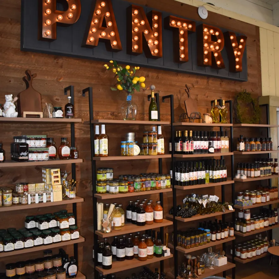 Rustic pantry shelves stocked with jars, bottles, and food items under illuminated marquee pantry sign.