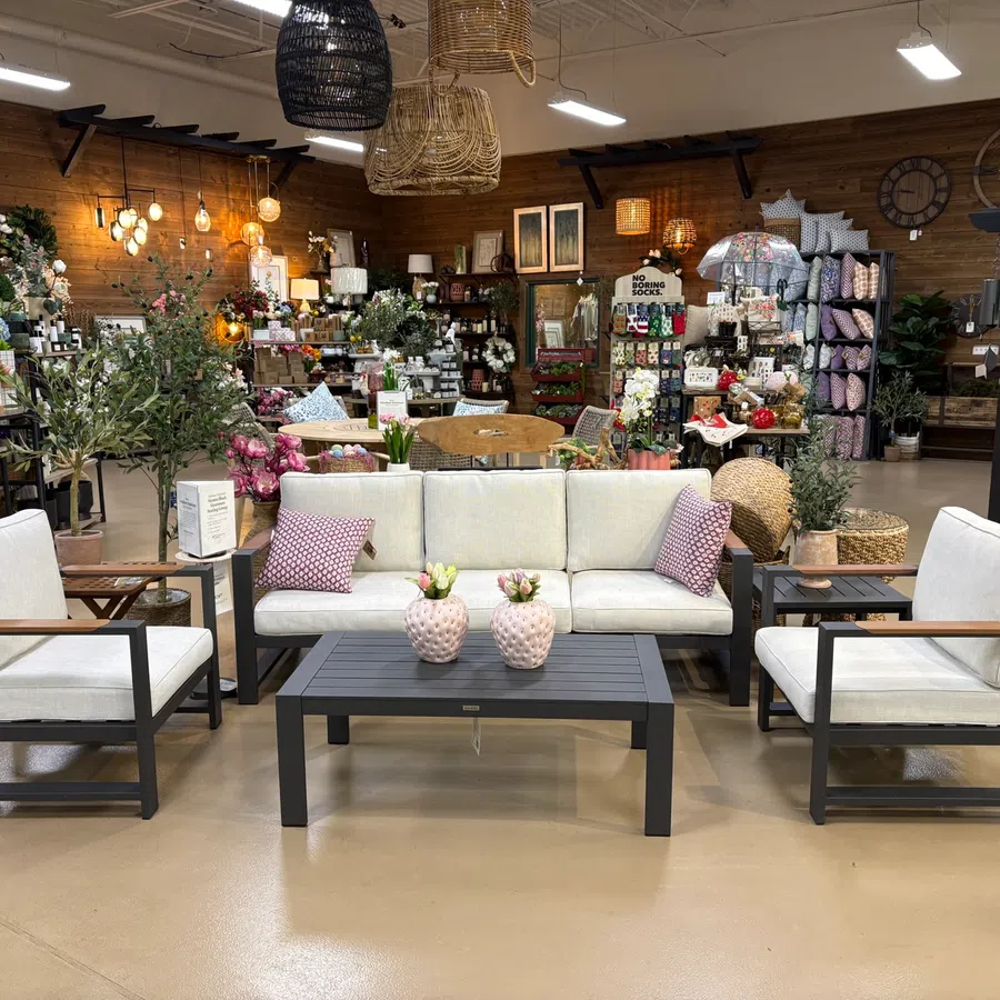 Modern indoor furniture set with white cushions and black frames in a home decor store with plants and decorations.