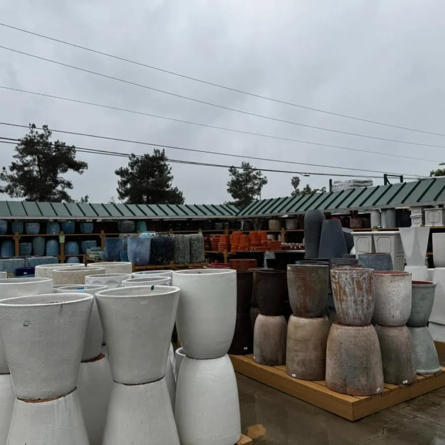 Outdoor display of various large ceramic pots and planters under overcast sky in a garden center