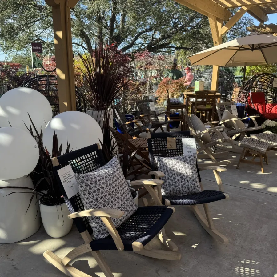 Outdoor patio furniture display with rocking chairs, cushions, plants, and large white decorative balloons under wooden pergola.