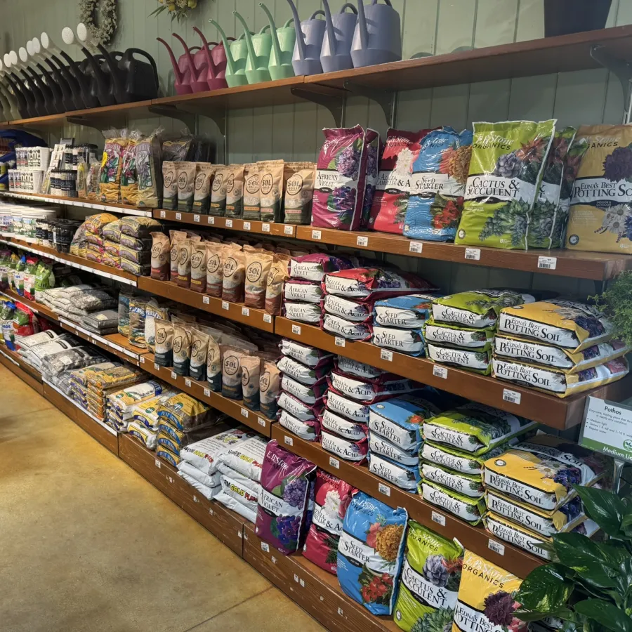 Retail store shelves stocked with various gardening soils, potting mixes, and gardening supplies in bags.