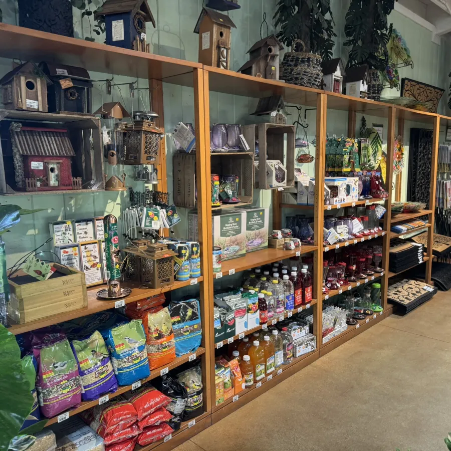 Wood shelves displaying birdhouses, bird feed bags, jars, and garden supplies in a rustic store setting.