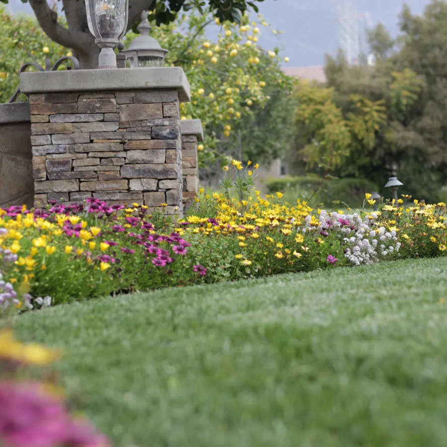 Well-maintained garden with colorful flowers bordering a green lawn and stone pillar with lanterns.