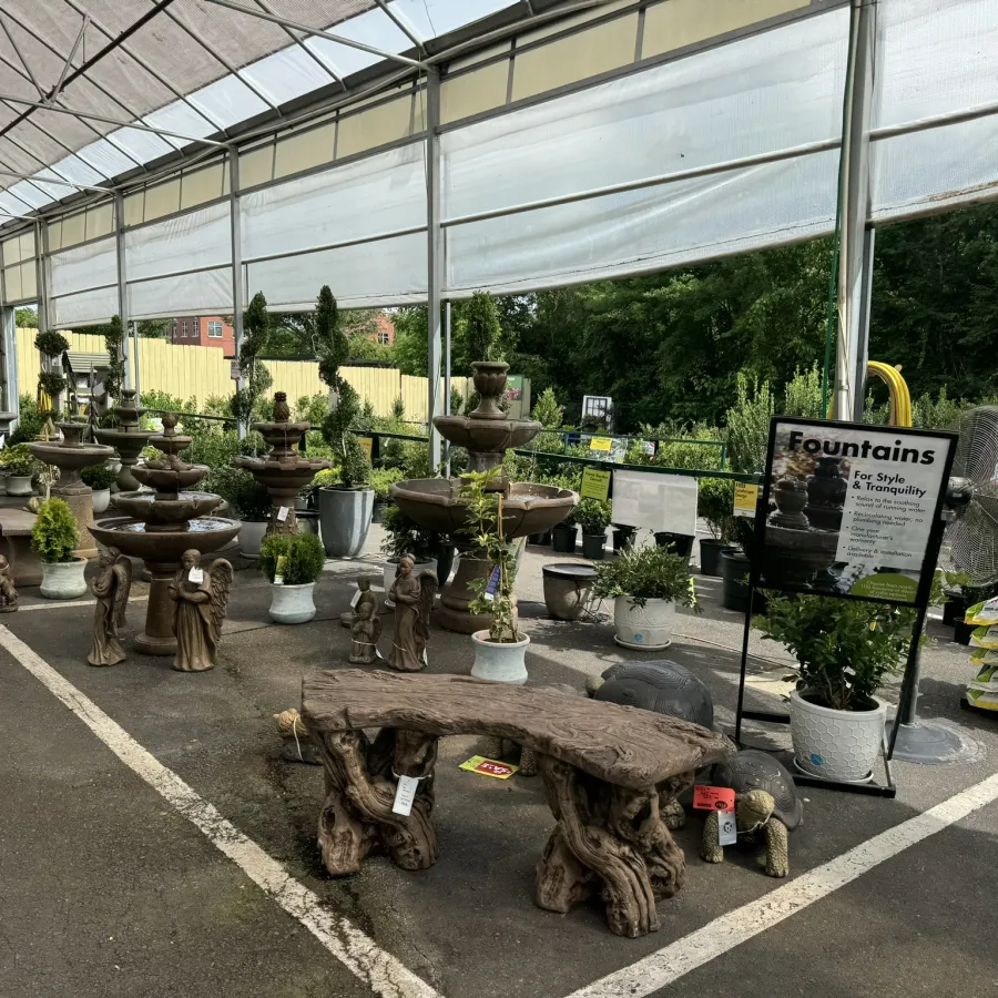 Outdoor garden center display of various stone fountains, statues, and decorative plants under a canopy.