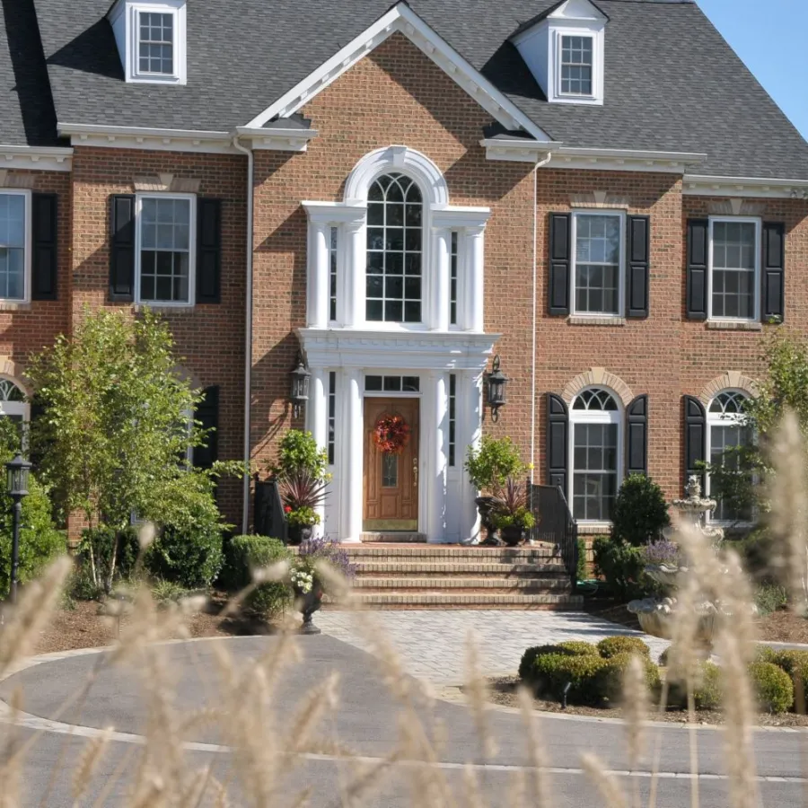 Two-story brick house with large windows, white trim, landscaped front yard, and clear blue sky.