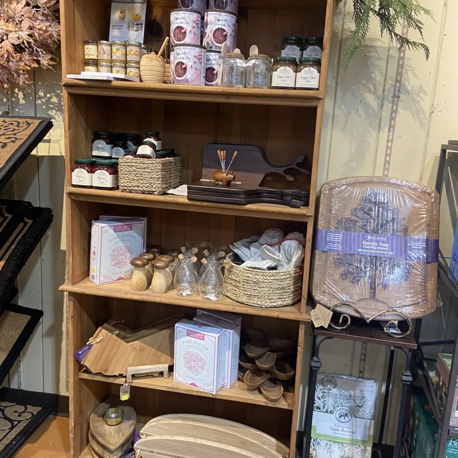 Wooden shelf displaying kitchen items including jars, spice containers, cutting boards, and decorative baskets in a store.