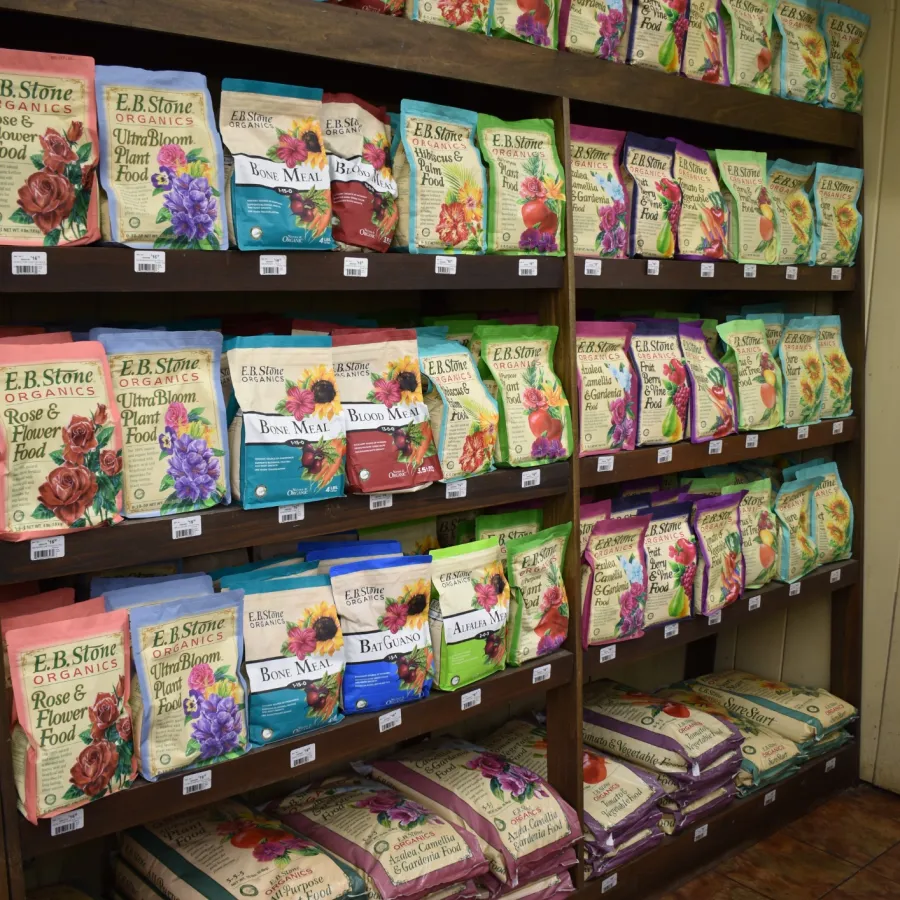 Shelf displays multiple colorful packets of E.R. Stone Flower Power organic gardening products with floral designs.