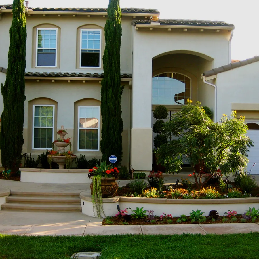 Modern two-story house with manicured garden, tall cypress trees, and decorative fountain by entrance.