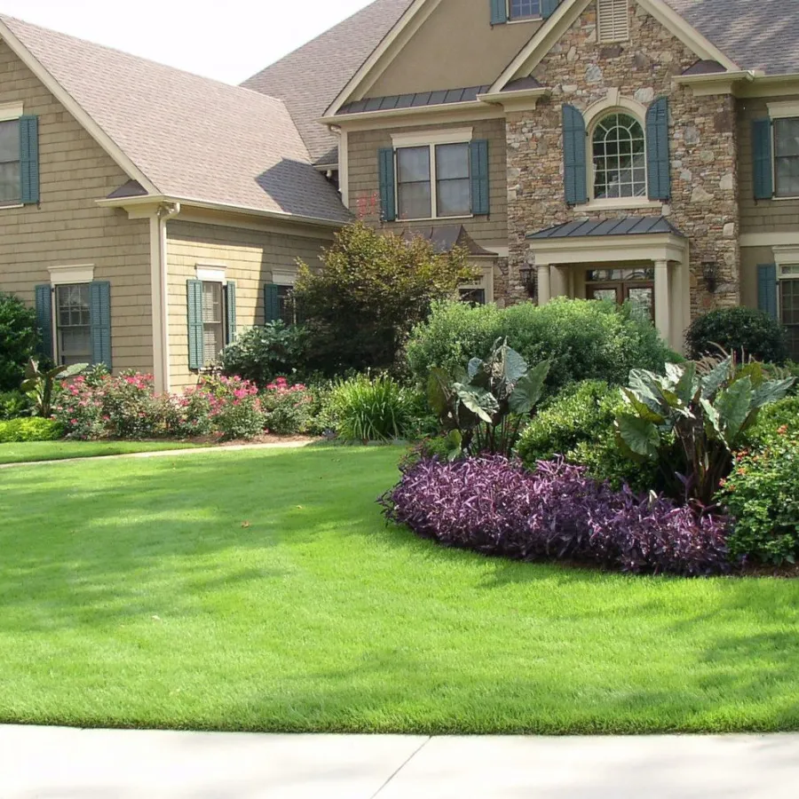 Large suburban house with stone and siding exterior surrounded by lush green lawn and colorful garden beds