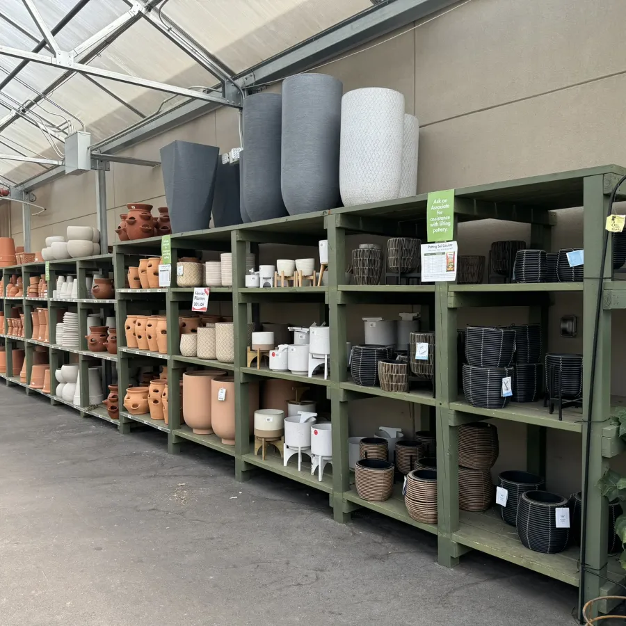 Shelves filled with various sizes and colors of ceramic and clay plant pots in a garden center aisle.