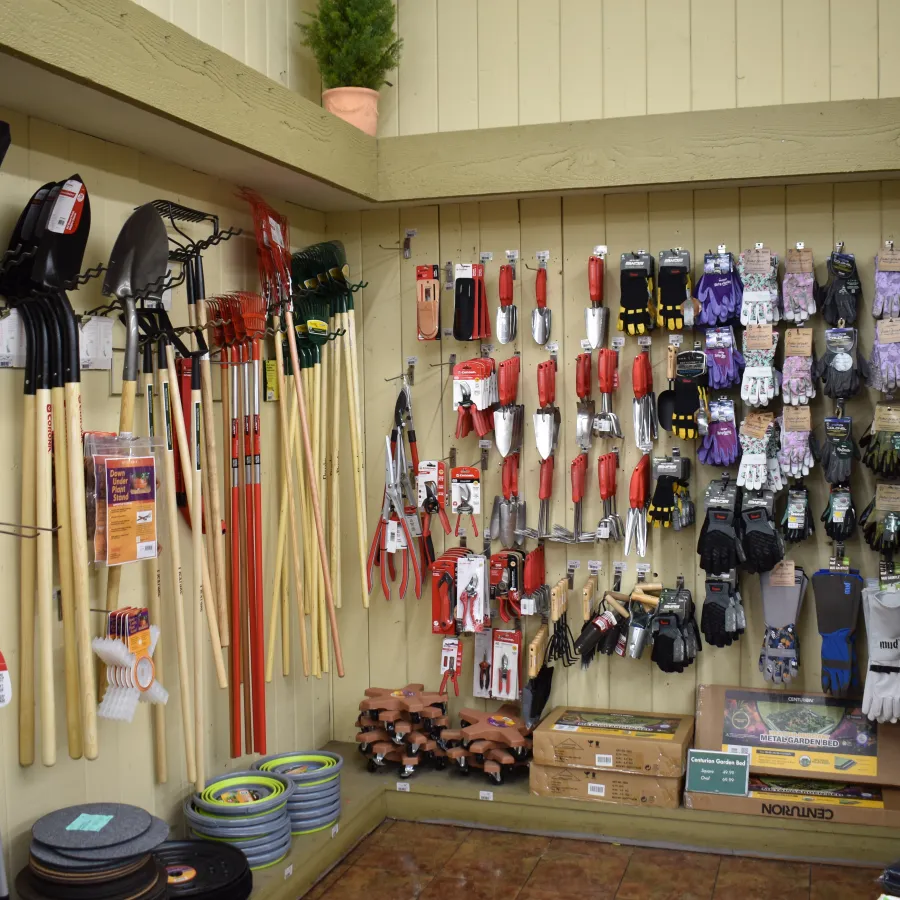 Wall display of gardening tools including shovels, rakes, gloves, and hats in a store corner.
