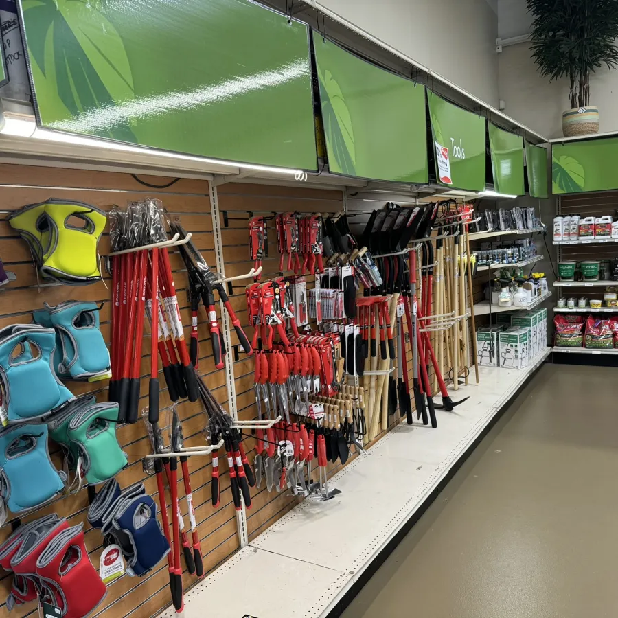 Garden tools and gloves displayed on shelves in a store aisle with bright green signage overhead