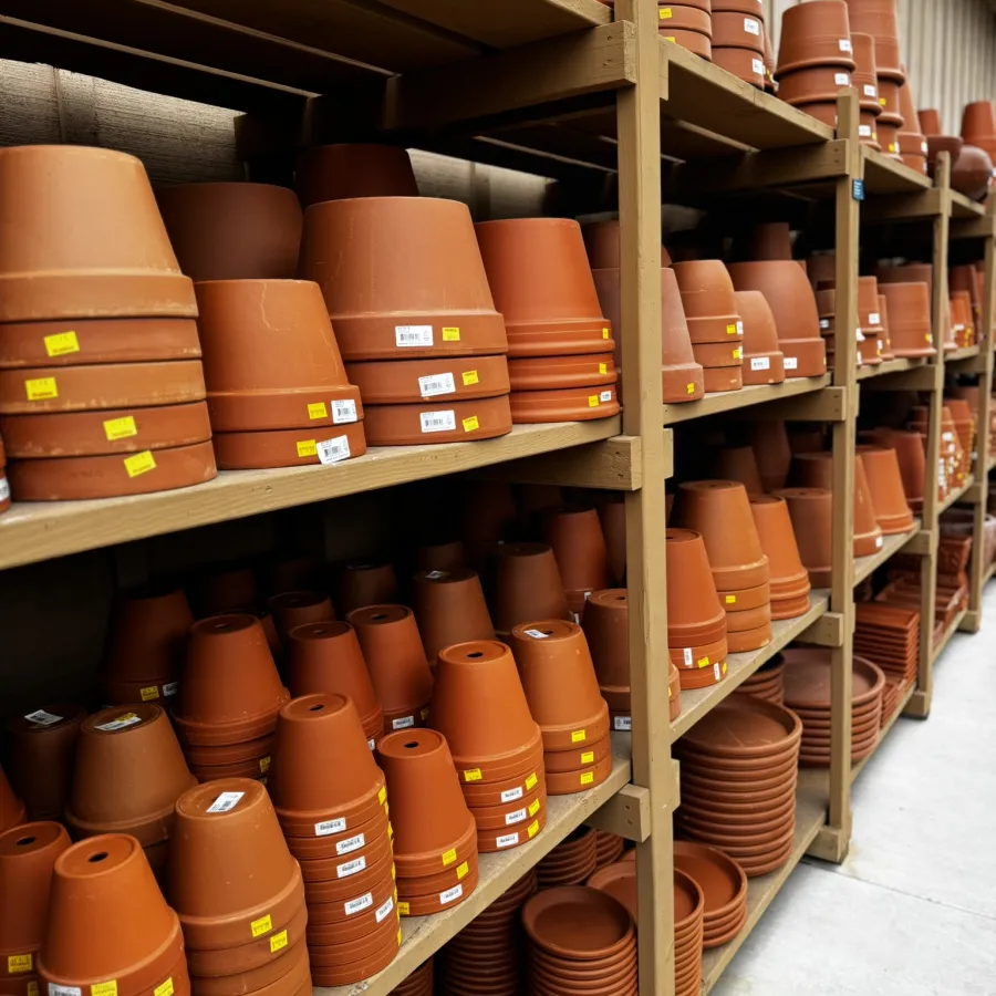 Rows of terracotta plant pots and saucers neatly stacked on wooden shelves in a garden store aisle.