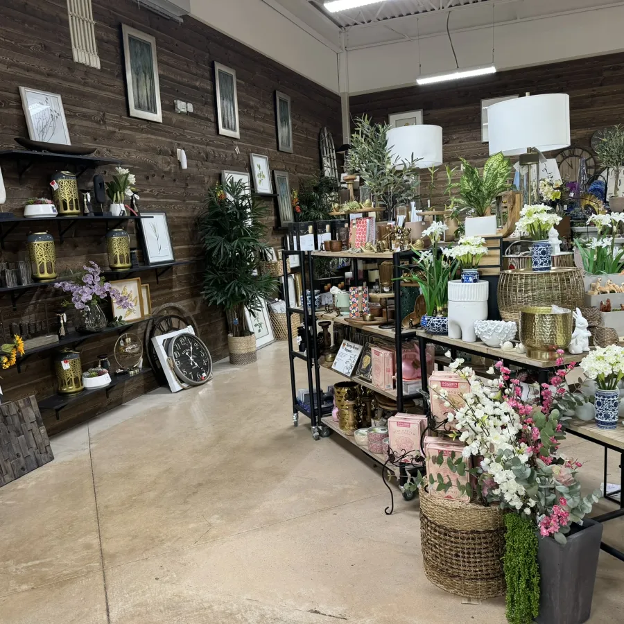Interior of a rustic gift shop with shelves displaying clocks, vases, flowers, and decorative items on a polished floor.