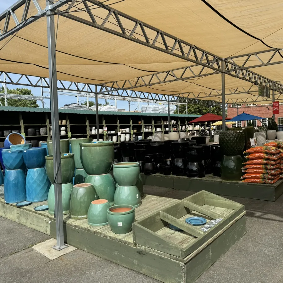 Outdoor garden center display of various colorful ceramic pots and bags of soil under shade structure