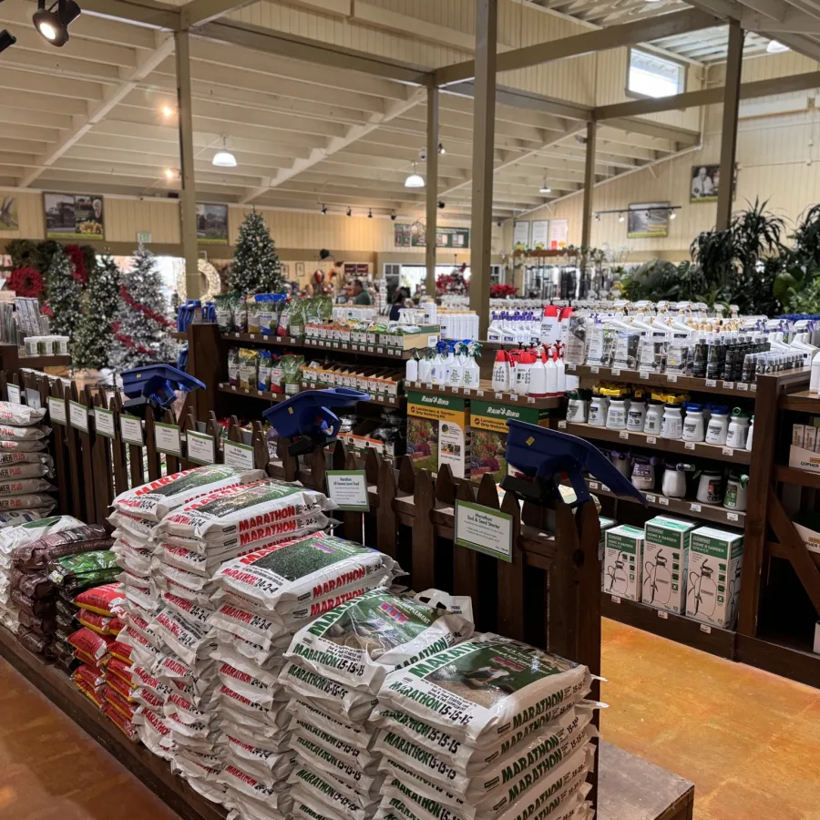 Indoor garden center aisle with stacked fertilizer bags, plant care products, and garden supplies under high ceilings.