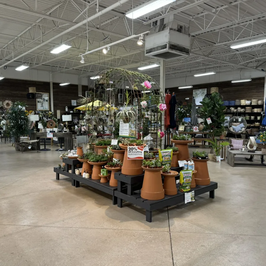 Indoor garden store display with terracotta pots, plants, and gardening supplies on wooden platforms under bright lights.