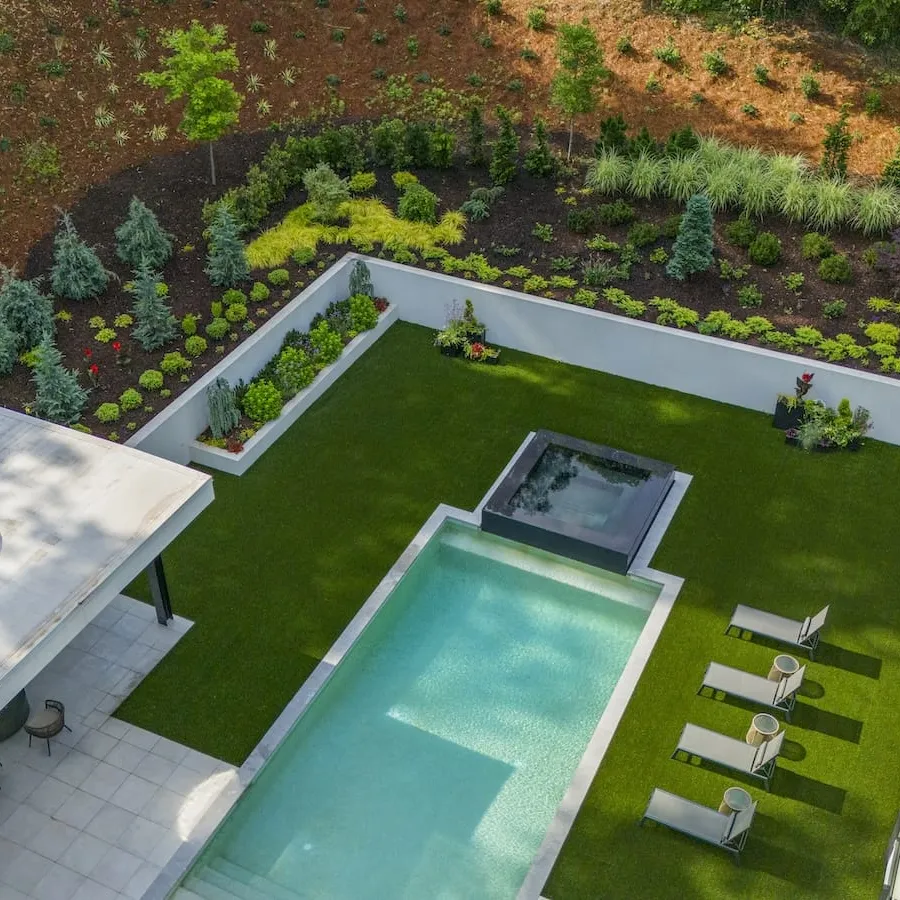 Aerial view of modern backyard with rectangular pool, hot tub, lawn chairs, and landscaped garden beds.
