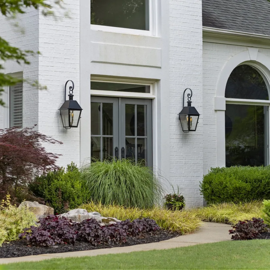 Modern white brick house entrance with black lanterns and landscaped garden featuring shrubs and ornamental grass.