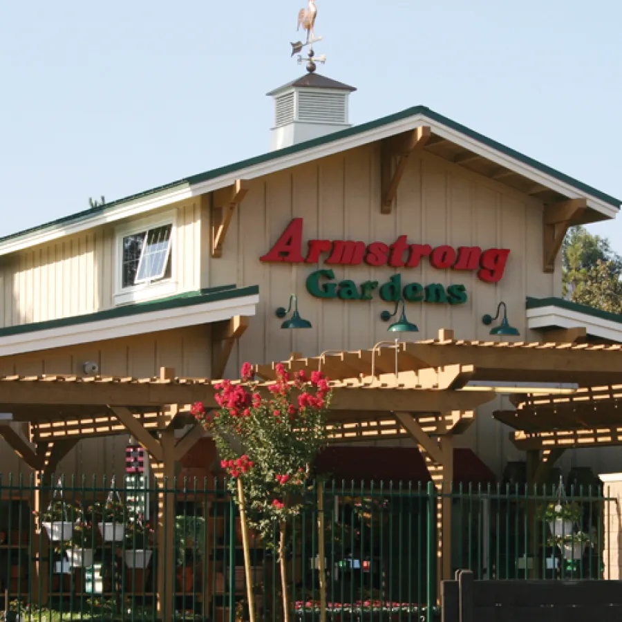 Armstrong Gardens building with wooden pergola, potted plants, and green traffic light in sunny outdoor setting.