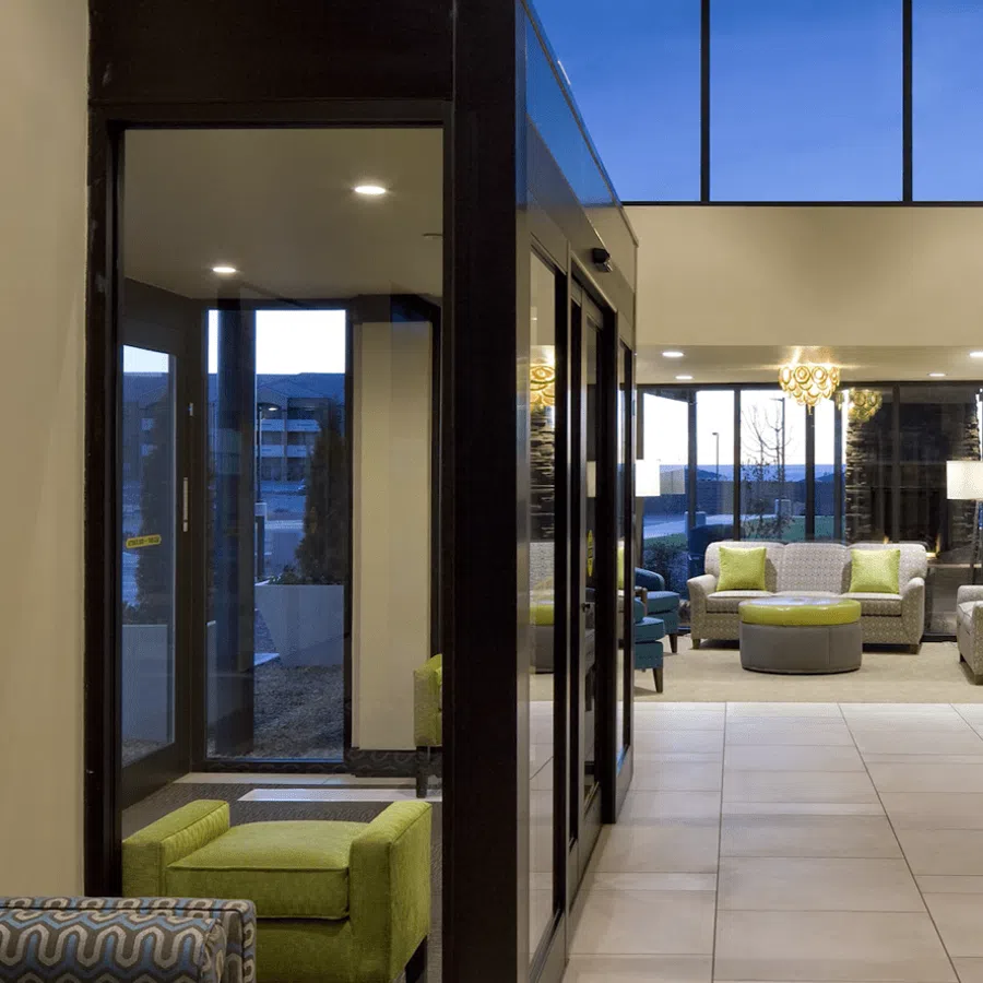 Modern hotel lobby with green and gray armchairs, large windows, and contemporary lighting at dusk.