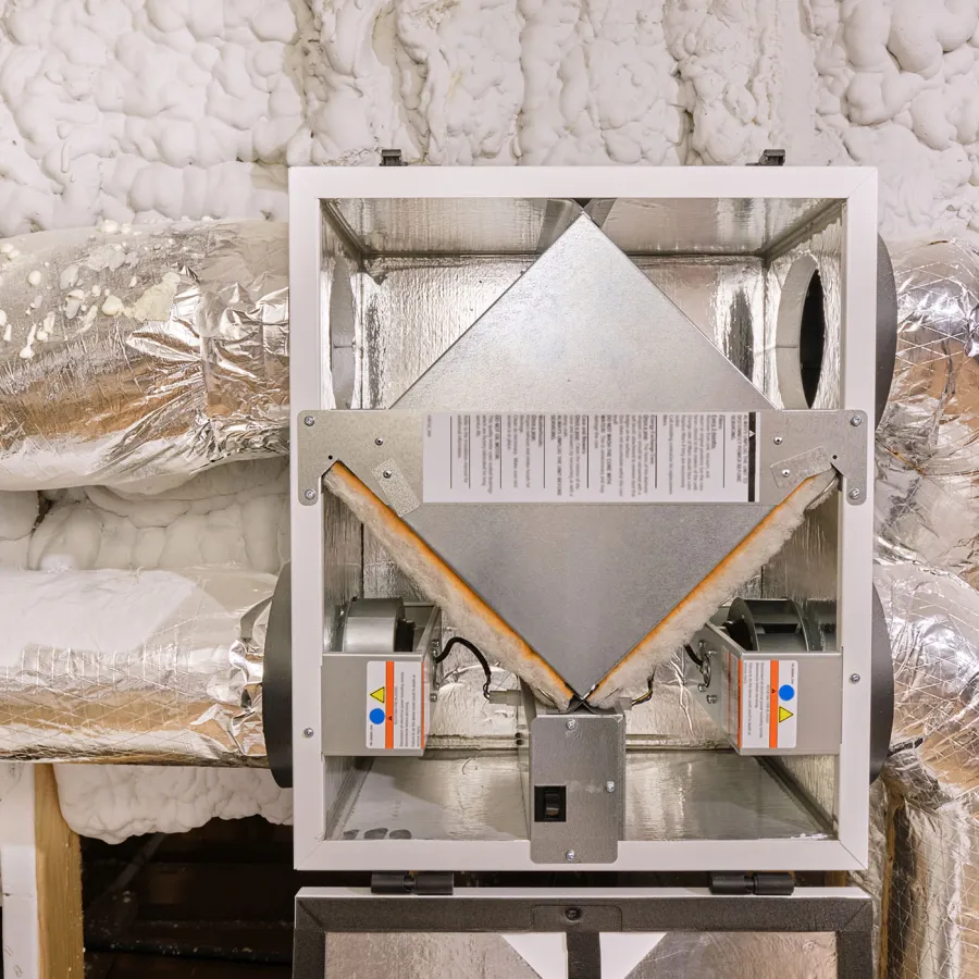 Ceiling-mounted heat recovery ventilator with insulated ductwork and spray foam insulation in attic space