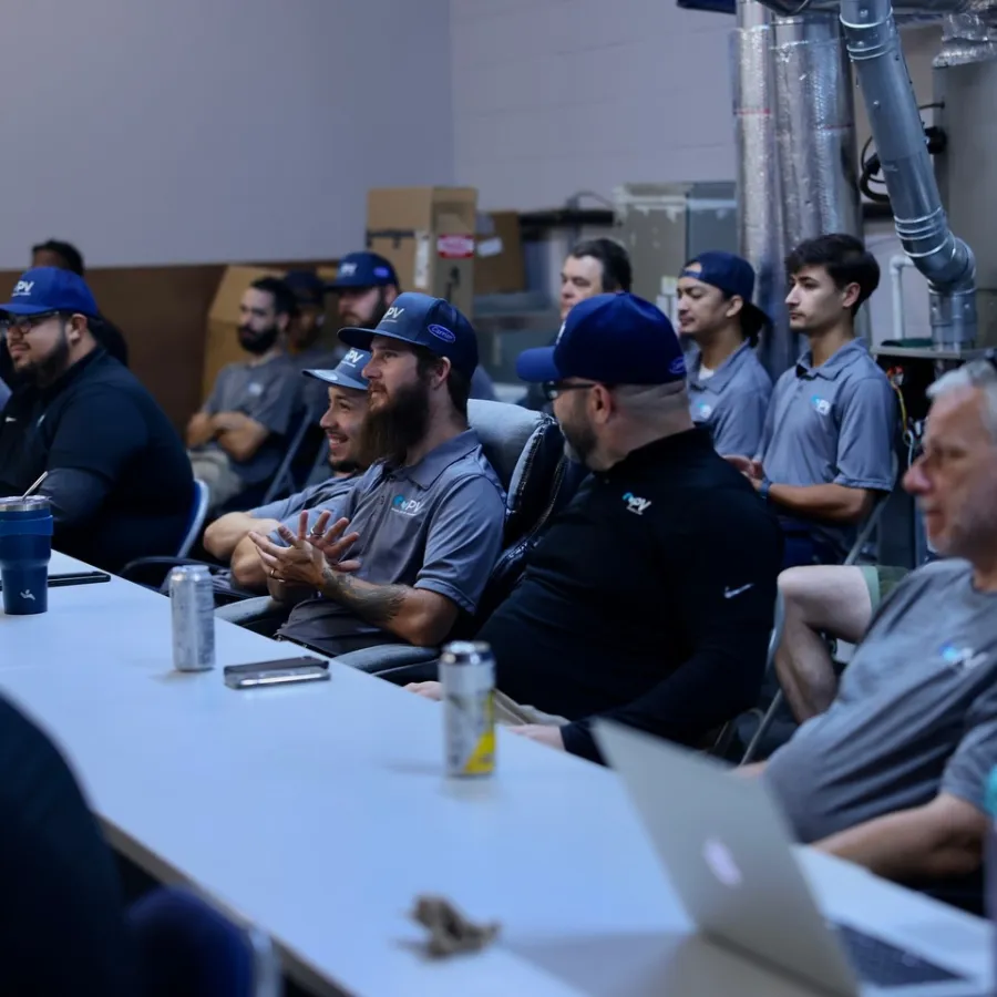 Group of men in casual attire sitting around a table during a meeting or workshop in an industrial setting.