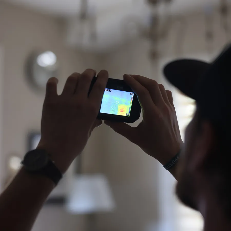 Person holding a thermal imaging camera inside a room capturing heat signatures of walls and objects.