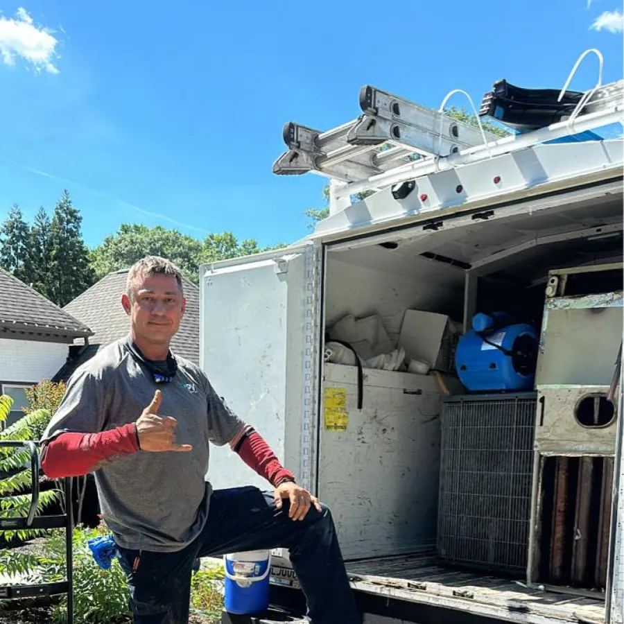 Man in workwear posing with hand gesture next to open work truck loaded with tools and equipment.