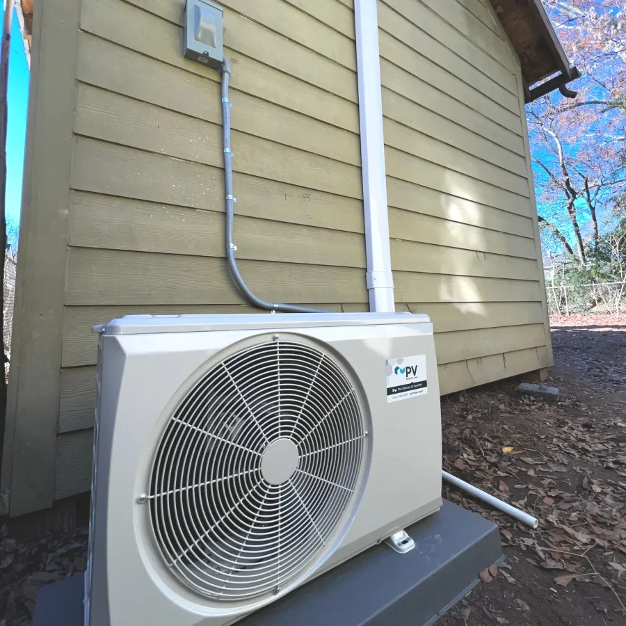 Outdoor heat pump unit installed beside a yellow wooden house on a concrete pad