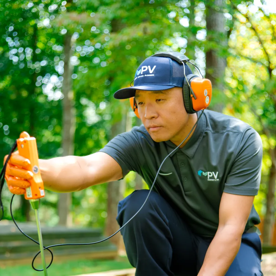 Man in uniform using soil testing tool on green grass wearing ear protection and orange gloves in park setting