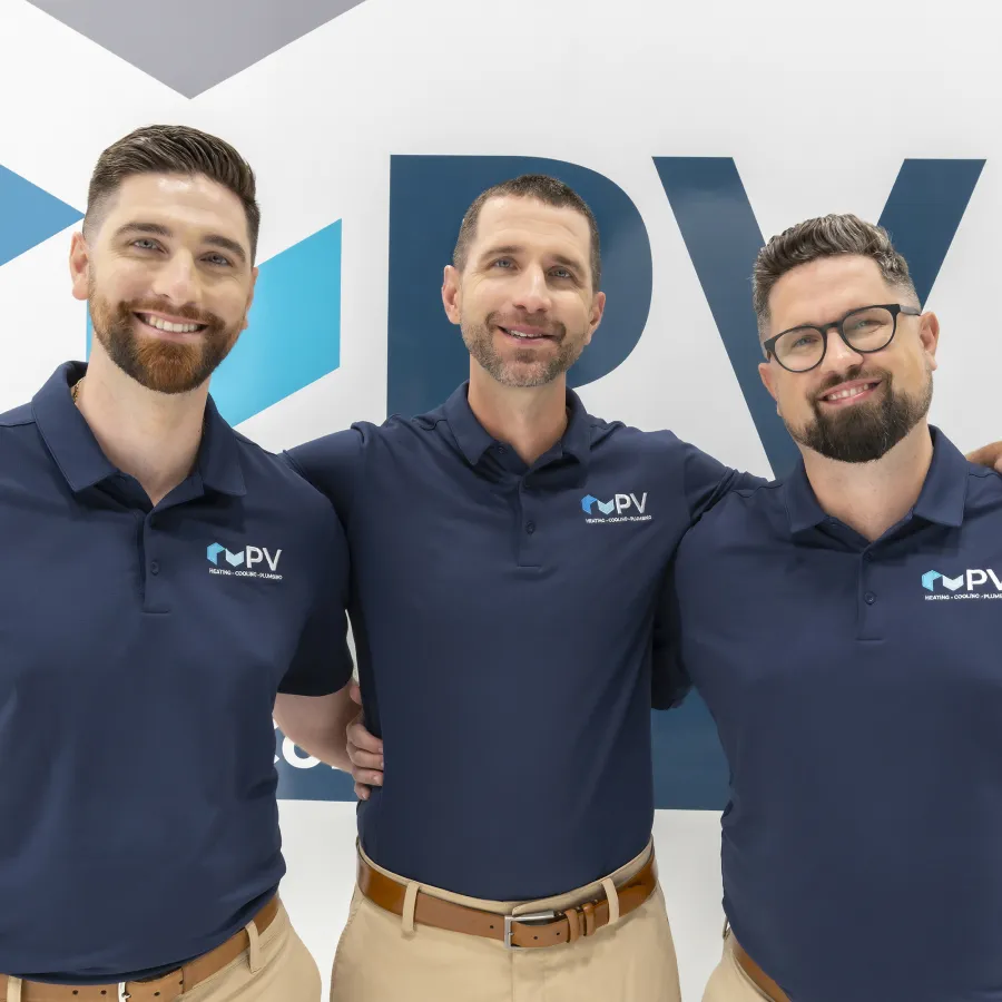 Three men in navy blue PV polo shirts posing and smiling in front of a PV branded background