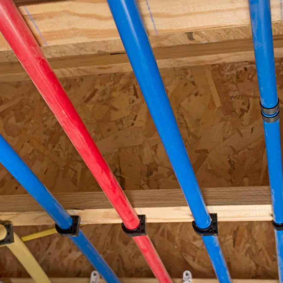 Red and blue plastic water pipes installed in wooden ceiling joists inside a building under construction.